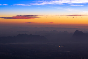 Obraz premium Mountains in clouds at sunrise in summer. Aerial view of mountain peak in fog. Beautiful landscape with high rocks, forest, sky. Top view from drone of mountain valley in low clouds. Foggy hills