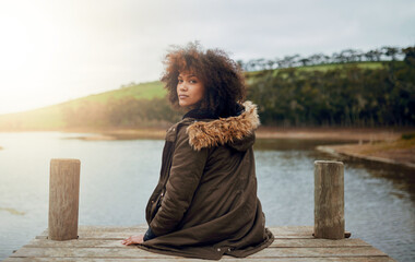 Enjoying natures quiet. Portrait of a young woman looking over her shoulder while sitting on a pier.