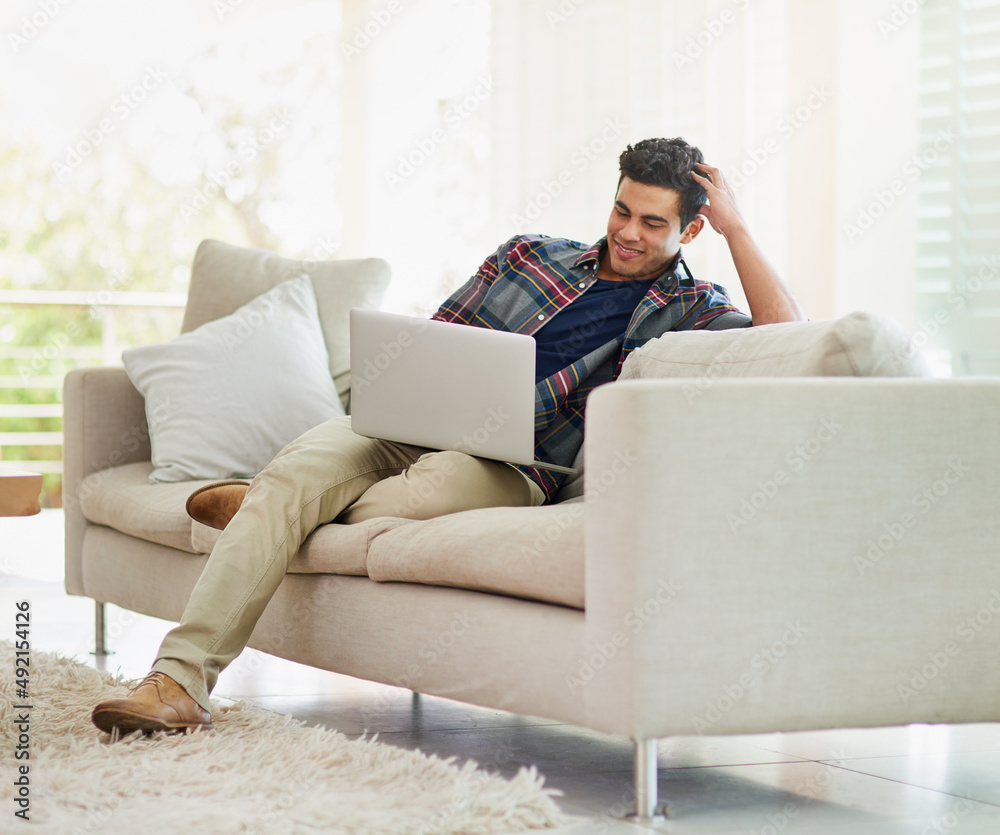 Poster comfortable and connected. shot of a handsome young man using his laptop while relaxing on the sofa 
