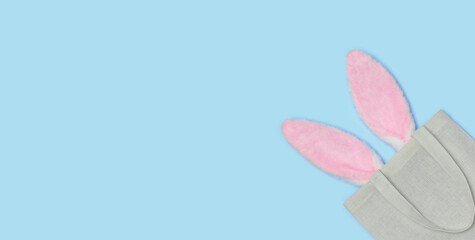 Banner. Pink Easter bunny ears sticking out of Reusable textile bag on a blue background. Happy Easter minimal concept. An Easter card with a copy of the place for the text. Flat lay