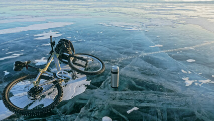Man and his bicycle on ice. He looks at the beautiful ice in the cracks. First-person view on bike. Nearby is a thermos and biking backpack. Ice of the frozen Lake Baikal.