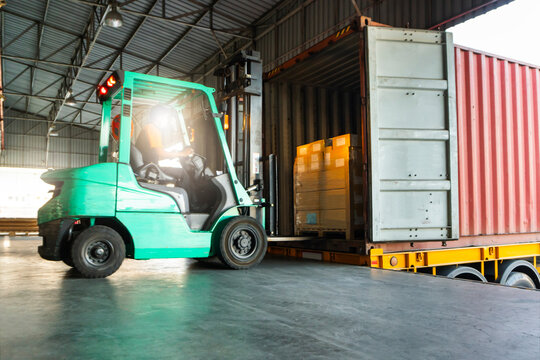 Forklift Tractor Loading Packaging Boxes on Pallets into Shipping Container at Dock Warehouse. Delivery Cargo Trucks Service. Distribution Warehouse Logistics. Shipment Freight Truck Transportation.