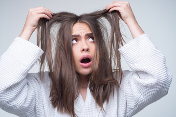 Fototapeta premium Sad woman looking at damaged hair, the hair loss problem. Studio isolated portrait, copy space.