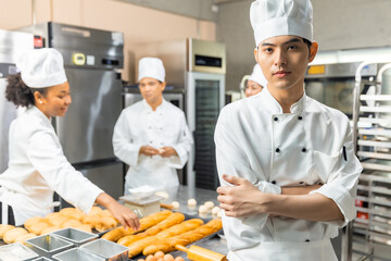 Smiling bakers looking at camera..Chef  baker in a chef dress and hat, cooking together in kitchen.Young asian man takes fresh baked cookies out of modern electric oven in kitchen.