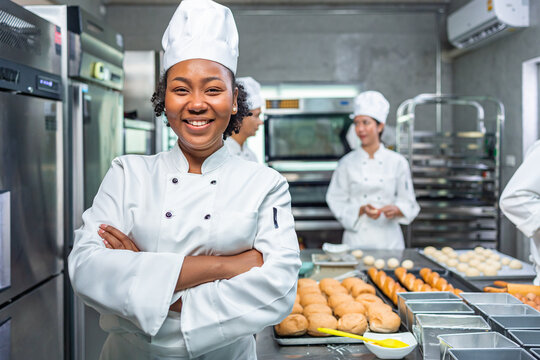 Smiling african  female bakers looking at camera..Chefs  baker in a chef dress and hat, cooking together in kitchen.Team of professional cooks in uniform preparing meals for a restaurant in  kitchen.