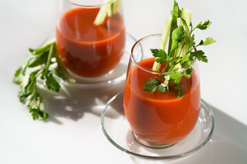 tomato juice with parsley and cucumber in glass glasses on a light background