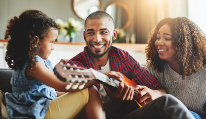 Tuned into family time. Shot of an adorable little girl and her parents playing a guitar together on the sofa at home.