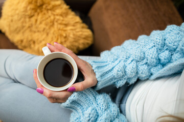 A mug of hot coffee in a woman's hands at home.