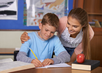 Every child is special. A supportive young teacher leaning over her student while he writes in a...