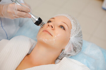 Close up portrait of a beautiful smiling woman relaxing during the RF lifting procedure in a modern beauty salon