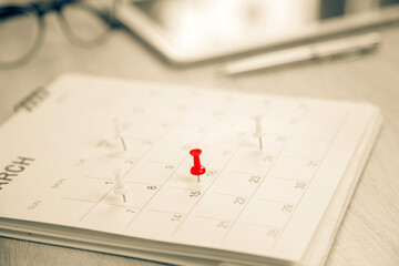 Close up pin on business desk calendar with office equipment concept of event planner or personal organization reminder and schedule or planning.