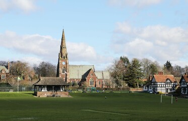 Fototapeta na wymiar The thatched cricket pavilion on the green at Thornton Hough, Cheshire, England, with All Saints Church in the background.