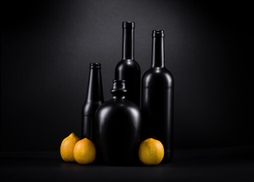obraz martwej natury z czarnymi szklanymi butelkami i żółtymi cytrynami na czarnym tle