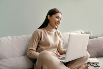 Beautiful young woman working with laptop on couch. Businesswoman using laptop managing her business.