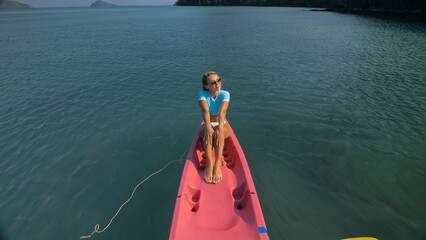 Pretty slim woman in elegant swimsuit lies in pink plastic kayak drifting on azure ocean at exotic resort upper view. Traveling to tropical countries. Girl is sailing on kayak in ocean, view above.