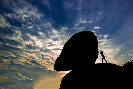 the silhouette of A woman pushed a large rock on the cliff under the beautiful and colorful sunset
