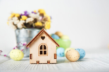 Happy Easter greeting card. Miniature wooden house. Rabbits, colorful eggs, spring flowers with tag for text..