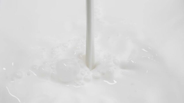 Slow motion stream of milk pours onto the milky surface and a funnel is formed.