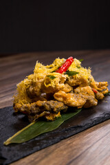 crispy deep fried salmon fish skin with salted egg yolk paste sauce on black stone plate wood table restaurant chinese banquet halal food asian cafe menu