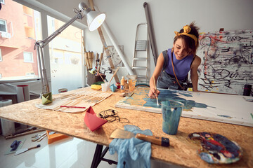 A young female artist is enjoying the process of creating a painting in the studio. Art, painting, studio