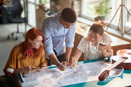 Young creative colleagues in the office are making changes to a guitar design