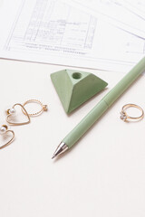 Fototapeta premium Green pen, jewelry and drawings on white background. Women's workplace. Female engineer, designer or architect