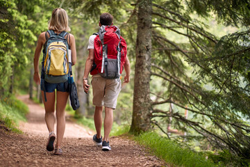 Man and woman with backpacks in forest on trail. Young couple together. Hiking, lifestyle, togetherness, nature concept