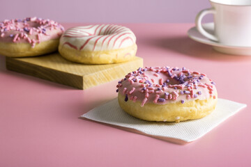 Three delicious fresh glazed donuts and porcelain cup for coffee or tea on pink background.Selective focus.