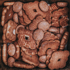 Pattern of biscuits of various shapes inside a square box of reflective tin