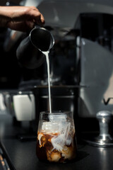 Ice coffee on a black table with cream being poured into it showing the texture and refreshing look of the drink
