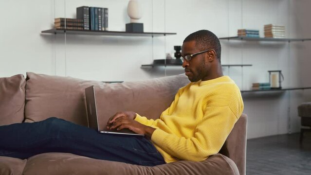 Young man working on a laptop on the couch. Man typing with laptop on couch