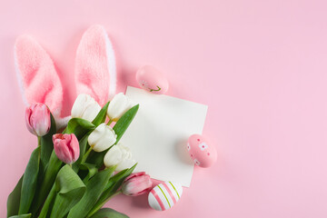 Easter background with easter eggs, fluffy bunny ears, spring tulips and empty card for text. Mockup.
