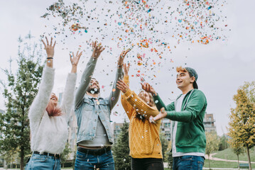 Multiethnic group of young students bonding outdoors, happy young people throwing confetti and...