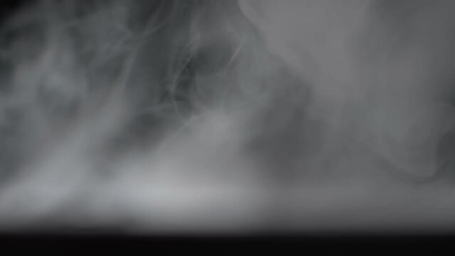 A white puff of smoke falls on a black background and fills the entire space. Smoke screen. Smoking.