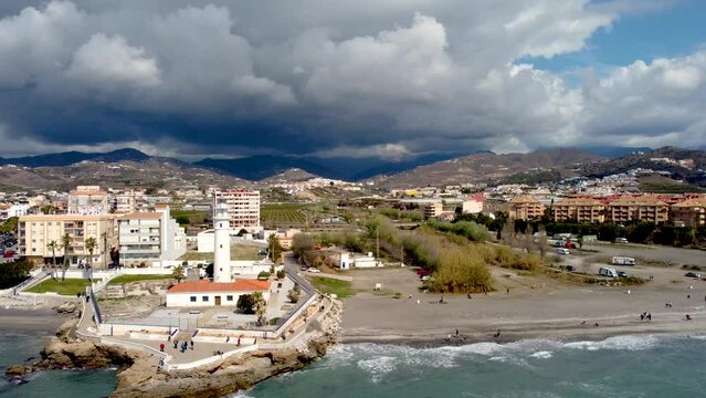 Panoramic aerial view of beautiful costal city Torrox. Drone panning left creating a beautiful circle around the lighthouse of Torrox. View of Torrox river and promenade of Torrox. Cloudy sky