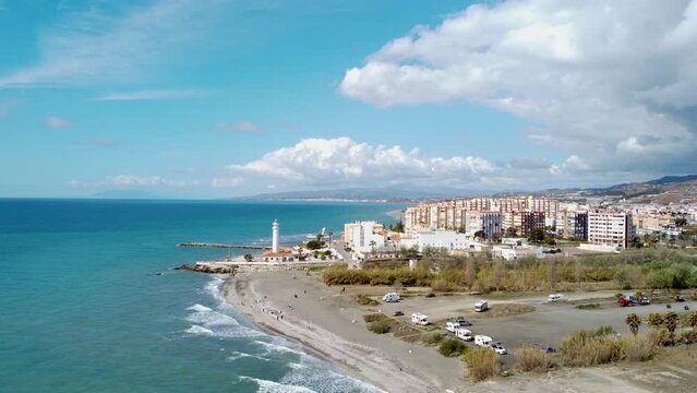 Panoramic aerial view of beautiful costal city Torrox. Drone panning left creating a beautiful circle around the lighthouse of Torrox. View of Torrox river and promenade of Torrox. Cloudy sky
