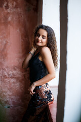 Fototapeta premium Portrait of a young charming woman with curly hair, fair-skinned girl in a black top and with a smile on her face. Curly woman in light clothes