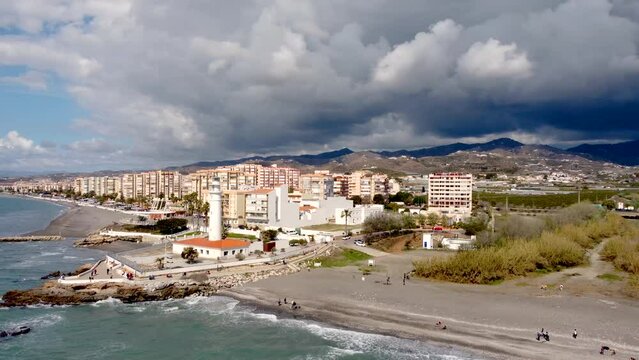 Panoramic aerial view of beautiful costal city Torrox. Drone panning left creating a beautiful circle around the lighthouse of Torrox. View of Torrox river and promenade of Torrox. Cloudy sky
