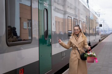 A young woman in a coat and with a bouquet of flowers is waiting at the train station. The girl is waiting for the train at the station in Europe.