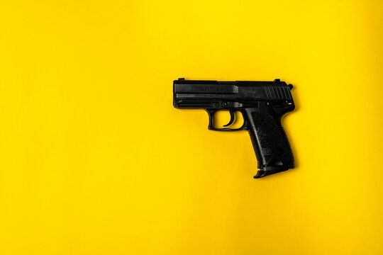 Short black gun on a yellow background. A close up image of a gun pointed sideways on a plain background with space.