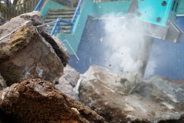 Blauer Betonbohrer aus Stahl über Betonfels Landschaft mit weißer Rauchwolke vor Betontreppe und...