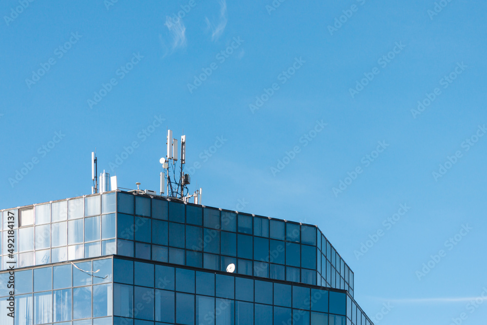 Wall mural a glass tiled building with an antenna on the roof top of it against a clear blue sky.