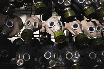 A full frame dark image of rows of gas masks with bright green filters on them and blue glass...