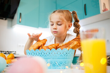 A little girl of 6-7 years old stands in the kitchen at the table and chooses a freshly baked bun. homemade baking