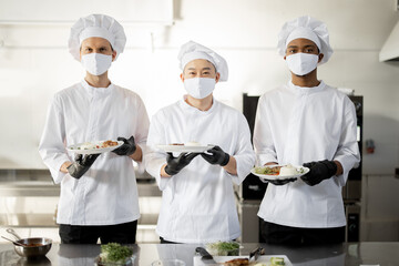 Portrait of multiracial team of cooks standing with ready meals for a restaurant in the kitchen....