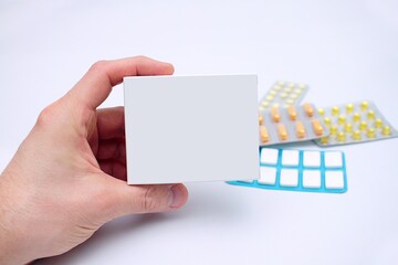 Pudełko prostokątne z lekiem trzymane w ręku mężczyzny na tle innych leków i na białym tle
