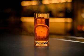 front view of tall glass full of cold alcoholic drink with orange slice on bar counter