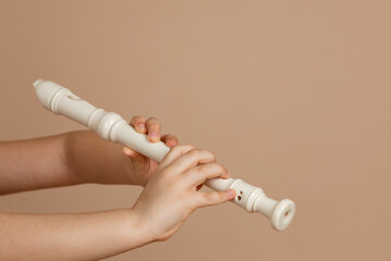 Hold fipple flute with both hands and pinch holes closeup, beige background. Woodwind musical...