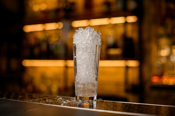 selective focus on tall glass full of ice pieces on bar counter