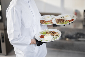 Chef holding three plates with ready meals, carrying them on hands. Cropped view without face, close-up. Concept of serving food for restaurant and haute cuisine